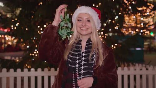 She holds up the mistletoe, smiling.