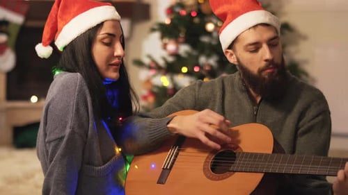 A couple singing with a guitar by the tree.