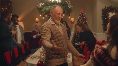 Grandfather opens his arms for a big hug, guests all around.