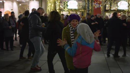 A crowd dancing in the street at night under lights.
