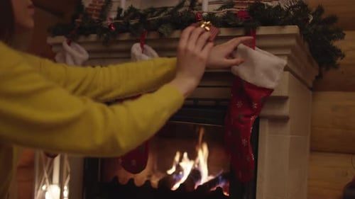 A hand hangs red stockings over the fire.