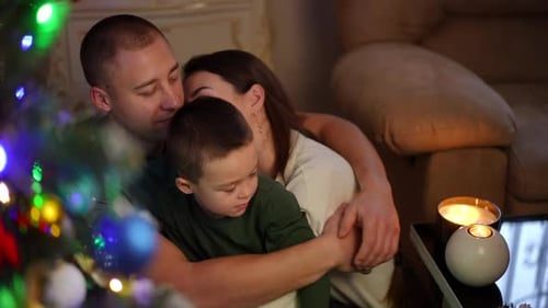 A boy hugs his dad by the tree.